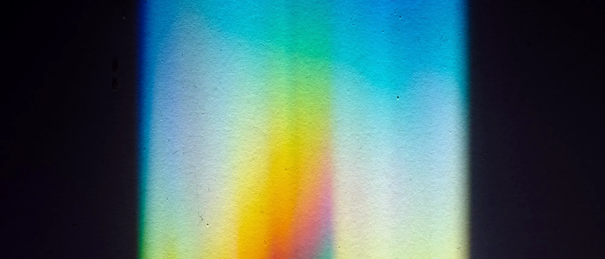 A prism splitting a beam of light into a spectrum across a dark wall.